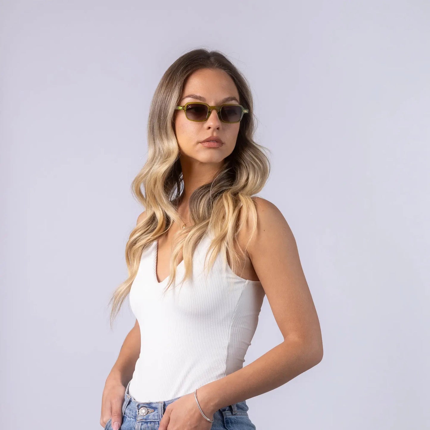 A female model wearing Exposure Sunglasses polarized sunglasses with green frames and tinted lenses, posing against a white background.